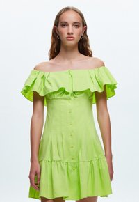 Vestido verde lima de un solo hombro con mangas con volantes, cierre de botones y diseño de falda escalonada. Fabricado con tejido ligero.