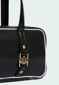 Czarna syntetyczna torba o teksturowanej powierzchni, z białym obszyciem i złotymi okuciami. Posiada wyraźną logo-klamrę oraz solidne czarne paski.