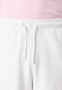 Pantalon de survêtement gris clair avec une taille élastique, doté d'un cordon de serrage. Le tissu semble doux et texturé.
