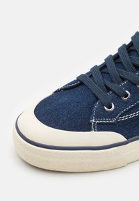 Mörkblå kanvas sneakers med vit gummisul, rund tå, vit söm och mörkblå snören trädda genom metallöglor.