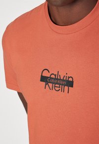 Calvin Klein CUT THROUGH LOGO - Apdrukāts T-krekls - copper sun