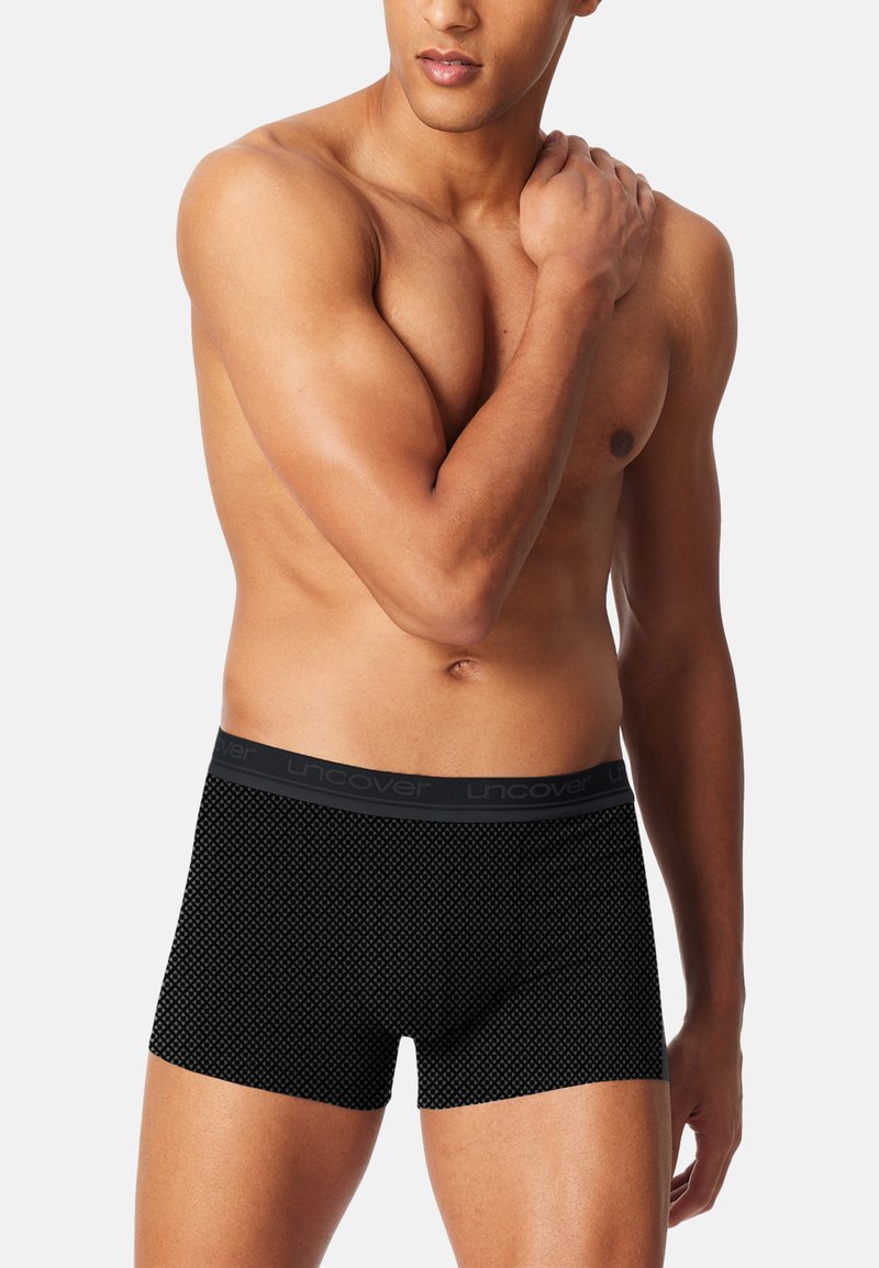 Black boxer briefs made of soft fabric, featuring a textured geometric pattern and a contrasting waistband with "Uncover" branding.