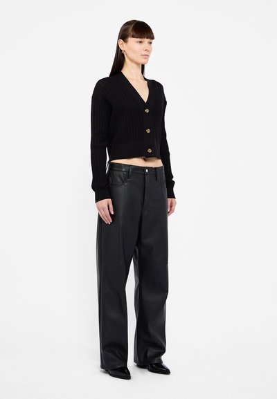Black ribbed cropped cardigan with a deep V-neck and gold buttons, paired with high-waisted black leather wide-leg pants.
