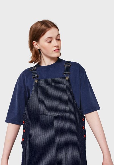Navy blue T-shirt paired with striped denim overalls featuring adjustable straps and red button accents on the sides.