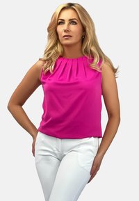 Fuksjowa bezrękawnikowa bluzka z plisowanym dekoltem, w zestawie z białymi dopasowanymi spodniami, prezentowana na jednolitym szarym tle.