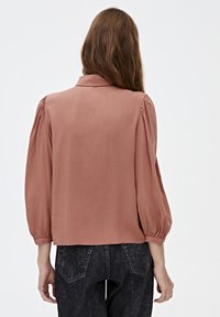 Rose-colored blouse with a collar and elasticated balloon sleeves. Back view shows a relaxed fit and smooth fabric texture. Paired with dark jeans.