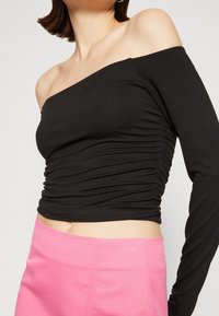 Svart off-shoulder topp med långa ärmar, rynkdetalj på sidan, tillsammans med en högmidjad rosa kjol. Mjuk tyg, passformande design.