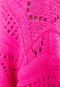 Sweter dziergany na drutach w jaskrawym różowym kolorze z fakturalnym wzorem, zawierający ażurowe elementy i miękkie, grube wykończenie.