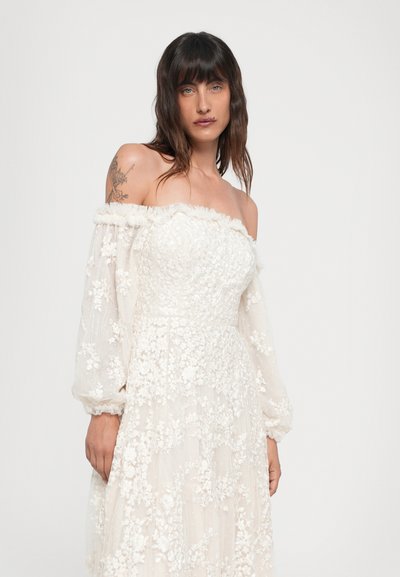 Vestido blanco sin mangas, con bordados florales texturizados, mangas transparentes largas y cuello con volantes. Fabricado en tejido suave y ligero con un diseño fluido.