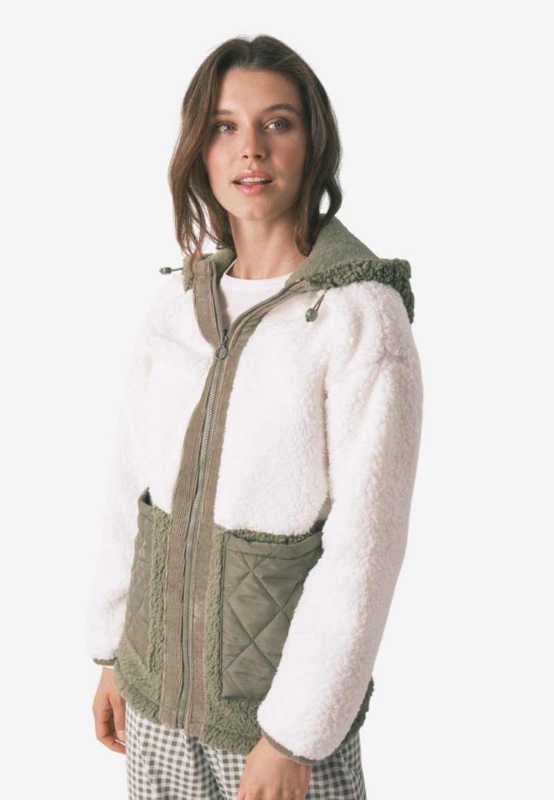 Giacca in pile con un corpo bianco, dettagli verde oliva, chiusura con zip, tasche trapuntate e cappuccio con fodera morbida e testurizzata.