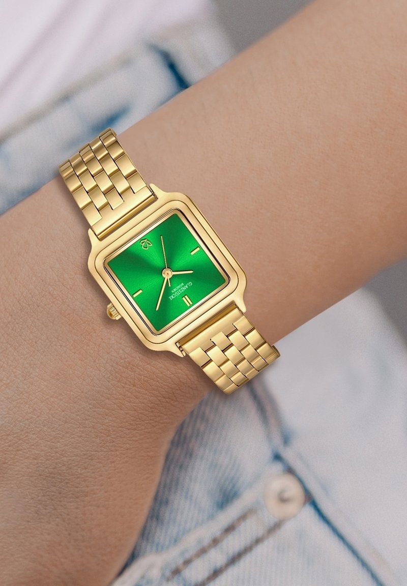 Ruudu kujuline kell rohelise kellanäidiku ja kullatooni metalsest rihmast. Omab minimalistlikku disaini, millel on tund, minut ja sekund käed.
