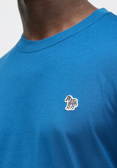 Niebieska bawełniana koszulka z okrągłym dekoltem, z haftem wielokolorowego konia w paski na lewej piersi. Gładka faktura.