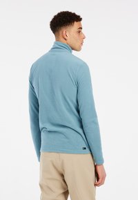 Pullover in pile blu con collo alto e maniche lunghe, caratterizzato da una texture morbida e un piccolo marchio sul bordo.