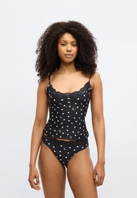 Mustast pitsiga kaunistatud tank-top valgete südamekujundustega, mille juurde kuuluvad sobivad mustad püksikud pitsdetailide ja sarnase südamekujundusega.