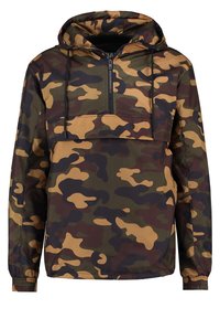 Chaqueta cortavientos de camuflaje con capucha, cierre de media cremallera en el frente, puños elásticos y una combinación de patrones en verde, marrón y beige. Material ligero.