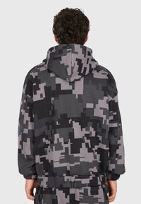 Bluza z kapturem w cyfrowym kamuflażu, z odcieniami szarości i czerni, o luźnym kroju i ściągaczami na końcach rękawów.