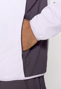 Biała i szara kurtka o miękkiej fakturze. Posiada boczną kieszeń i elastyczne mankiety. Projekt sportowy w kontrastujących kolorach.