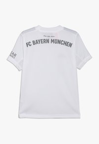 Camiseta blanca del FC Bayern Múnich con letras grises, mangas cortas y una textura de malla. "Mia san mia" está impreso sobre el logo.