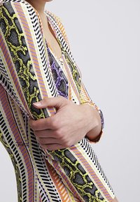 Färggad långärmad plagg med orms- och randmönster i gult, svart, lila och orange. Mjuk textur och figursydd design.