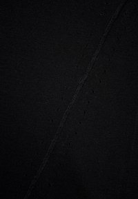 Černá látka s texturálním vzorem malých vystouplých puntíků, doplněná viditelným švem vytvářejícím diagonální čáry. Měkký a elastický materiál.