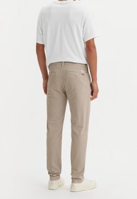 Beiga bomullbyxor med rak passform, med bakfickor och subtil logotypdetalj, i kombination med en enkel vit t-shirt och ljusa sneakers.