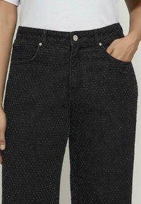 Czarne dżinsy z denimu z teksturowanym wzorem, pokryte wypukłymi kropkami, klasyczny krój pięciu kieszeni, zamek błyskawiczny oraz srebrne akcenty metalowe.
