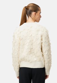 Kremfarvet sweater med tekstureret stof, prydet med 3D blomsterapplikationer. Ribstrikkede manchetter og kant, afslappet pasform og lange ærmer.