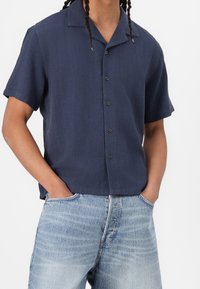 Camisa de manga corta azul marino, confeccionada con tela ligera, que presenta un cuello tipo camp y un corte relajado, combinada con unos vaqueros de denim azul claro.