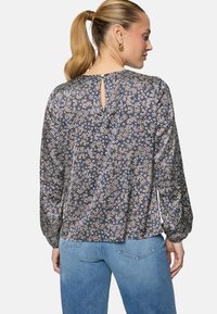 Femme avec une queue de cheval portant un chemisier à manches longues bleu marine à motifs floraux, avec une fermeture boutonnée en forme de trou à l'arrière, associé à un jean bleu clair.