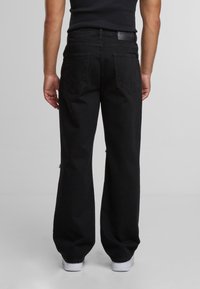 Mustad denimpüksid laiade säärtega, millel on kaks tagumist lisa taskut ning veidi kulunud tekstuur. Valged tennised täiendavad outfitti.