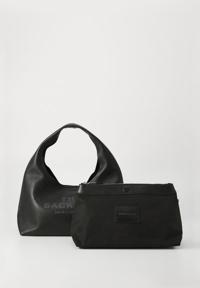 Deux sacs Marc Jacobs noirs sur une surface blanche : un sac hobo texturé avec une poignée courbée et une petite pochette zippée avec des finitions en cuir.