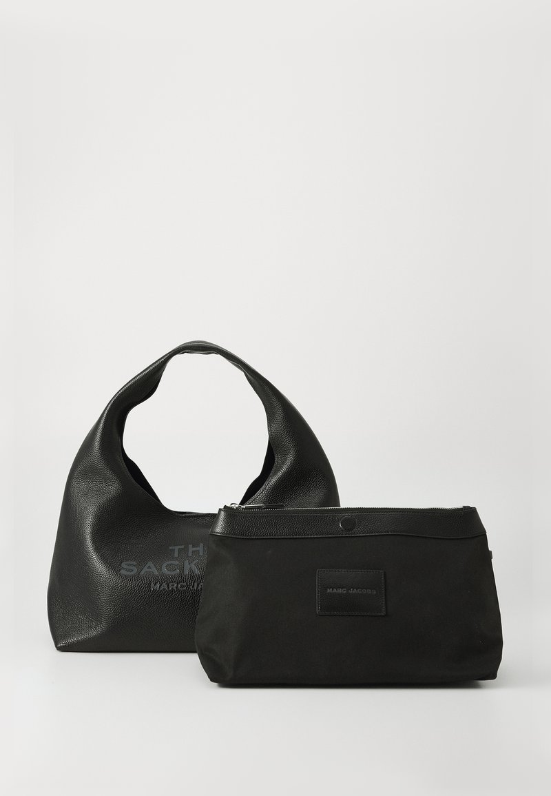 Duas malas pretas da Marc Jacobs sobre uma superfície branca: uma mala hobo texturizada com alça curvada e uma pequena bolsa com fecho zip e acabamento em couro.
