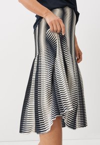 Gonna plissettata a righe blu navy e crema con orlo svasato. Il materiale ha una consistenza morbida, con linee orizzontali e verticali in un motivo ritmico.
