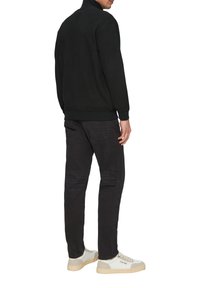 Schwarzer Strick-Zip-up-Pullover mit hohem Kragen, kombiniert mit dunkelgrauen Jeans und weißen Sneakers mit hellbeigen Akzenten und Logo.