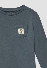 Donkergrijze longsleeve babyshirt met ronde hals en twee schouderknopen, met een klein zakje waarop een leeuwenillustratie staat.