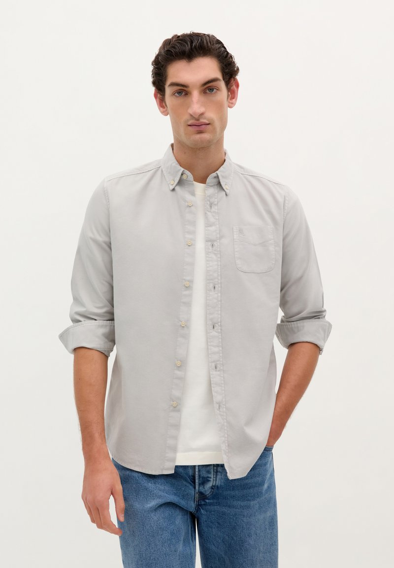 Cămașă button-up gri deschis, confecționată din bumbac, cu un buzunar la piept, mâneci suflecate și guler clasic. Asortată cu blugi din denim.