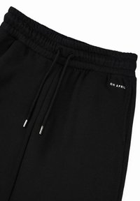 Pantaloni della tuta neri con vita con cordoncino, punte metalliche e testo bianco "OH APRIL" sulla parte anteriore. Realizzati in un morbido tessuto testurizzato.