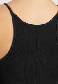 Top de tanque negro con relieve, que presenta tirantes finos y un escote trasero redondeado, con tela texturizada visible y detalles de costura mínimos.