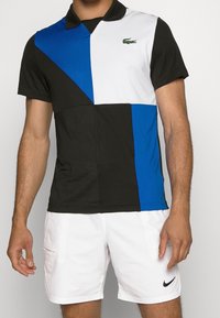 Polokrage t-shirt med kort ärm som har en geometrisk färgblockdesign i svart, vitt och blått med en strukturerad finish och logotypdetalj i grön.