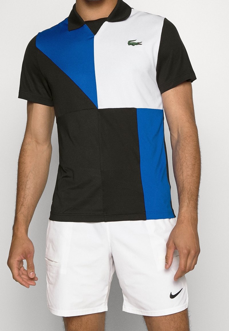 Polokrage t-shirt med kort ärm som har en geometrisk färgblockdesign i svart, vitt och blått med en strukturerad finish och logotypdetalj i grön.