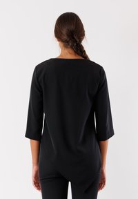 Top nero con maniche 3/4, texture liscia, scollo rotondo e orlo asimmetrico. Progettato per una vestibilità comoda e un utilizzo versatile.
