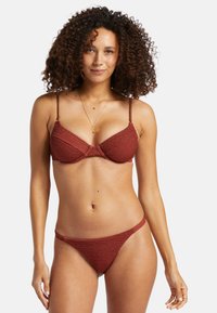 Červený textúrovaný bikiny set s trojuholníkovým vrchným dielom a zodpovedajúcimi spodnými nohavičkami so šnurovaním na bokoch. Nastaviteľné ramienka s minimálnymi kovovými prvkami.