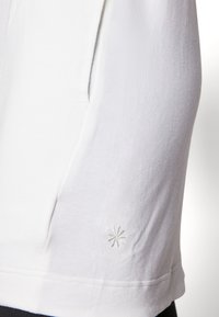 T-shirt bianco in cotone con una texture morbida, caratterizzato da un piccolo dettaglio di stella ricamata all'orlo e una tasca laterale per praticità.