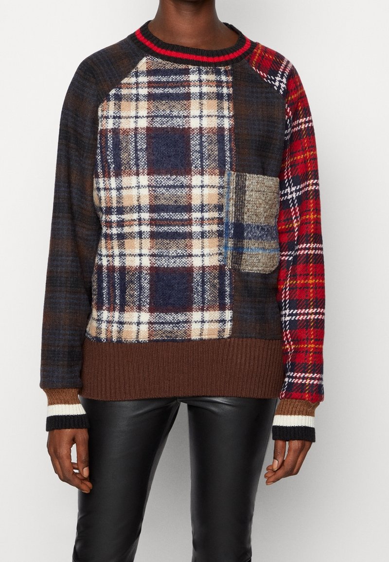 Personne portant un pull patchwork à carreaux multicolore avec ourlet et poignets côtelés marron, associé à un pantalon en cuir noir.