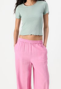 Světle zelený žebrovaný crop top s krátkými rukávy a vlnitým lemem, doplněný volnými růžovými kalhotami s elastickým pasem.