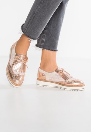 Roze gouden oxford schoenen met een glanzende afwerking, franjes en een kanten strik, gecombineerd met versleten grijs denim. Chunky witte zool.