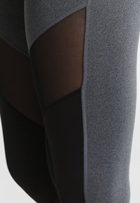 Leggings in un tessuto grigio texture con accenti neri. Presentano pannelli in rete ai lati per favorire la traspirabilità. Design a vita alta.