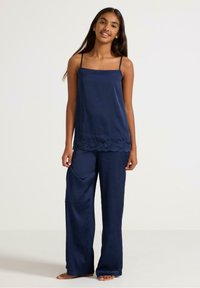 Navy silk camisole with thin straps, lace trim at hem, paired with loose-fitting navy silk trousers featuring side pockets.