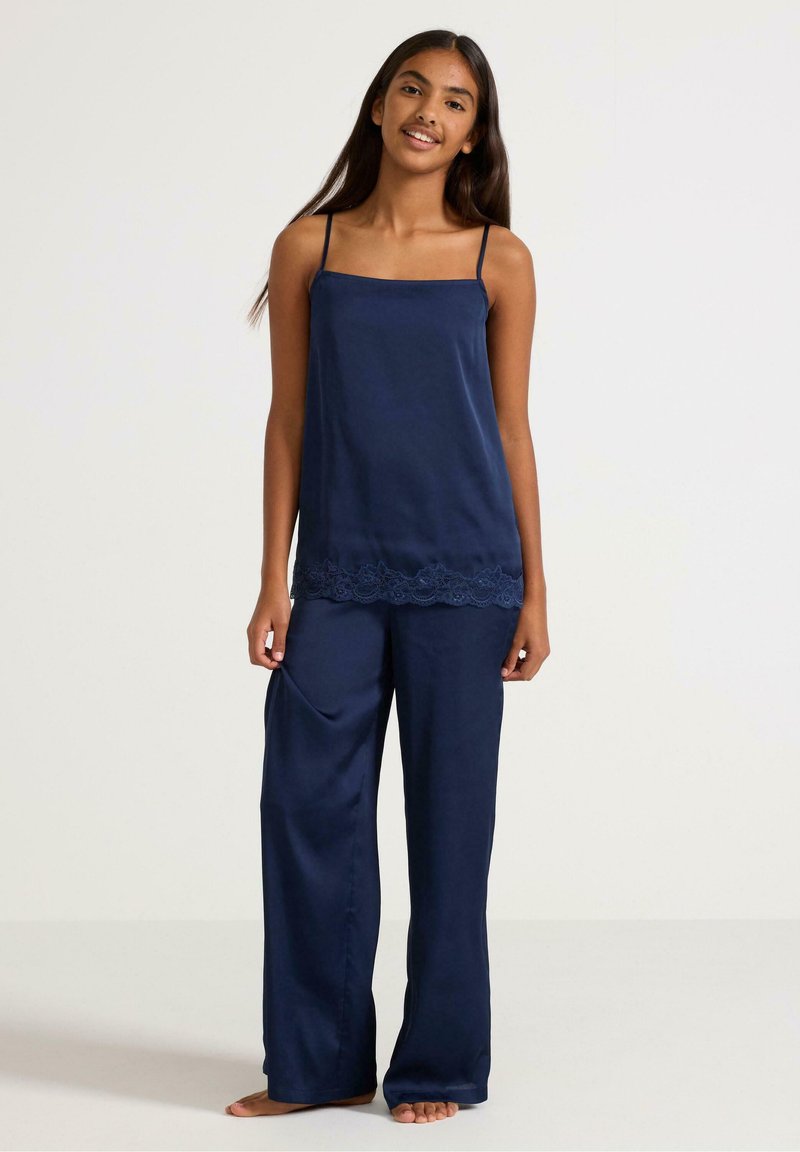 Navy silk camisole with thin straps, lace trim at hem, paired with loose-fitting navy silk trousers featuring side pockets.