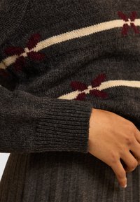 Maglione lavorato a maglia grigio scuro con una striscia crema e motivi floreali bordeaux. Polsini a costine, texture morbida, design aderente.